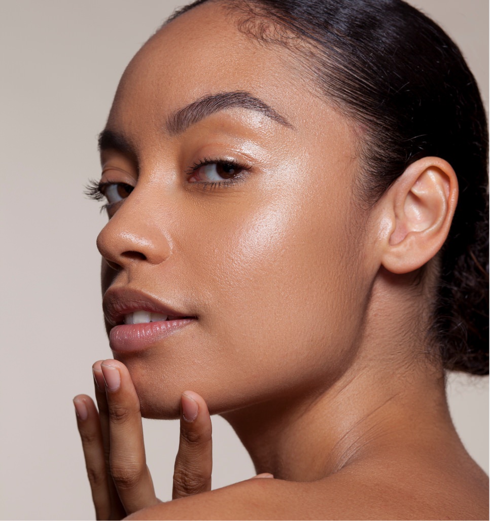 Black woman with hair pulled back gently touching her chin in a close-up skincare portrait.